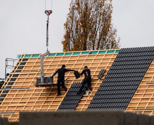 Two roofers laying new tiles on battens